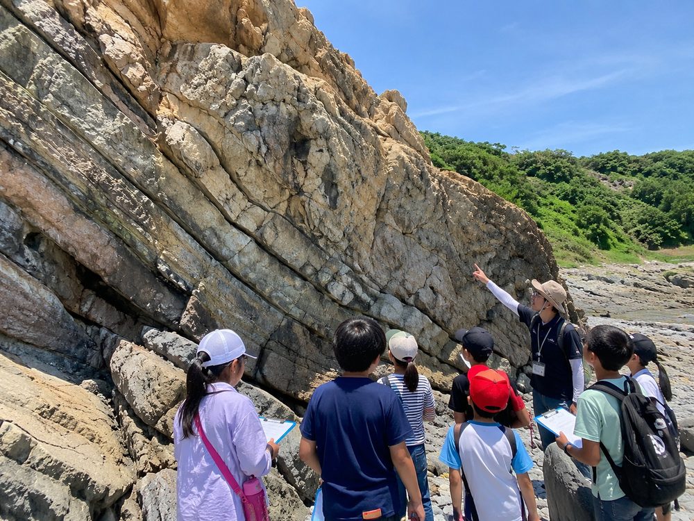 海辺の崖の地層を観察する子どもたち